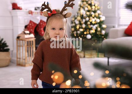 Une petite fille adorable portant un serre-tête de cerf dans la chambre décorée pour Noël Banque D'Images