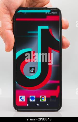 Un homme tient un smartphone, avec un fond d'écran TikTok et une icône d'application TikTok sur l'écran du téléphone portable Banque D'Images
