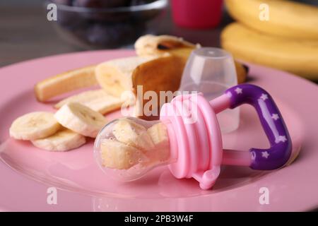 Grignoteuse avec banane et fruits frais sur plaque rose, gros plan. Alimentation bébé Banque D'Images