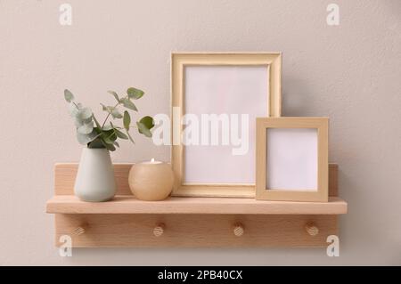 Étagère en bois avec cadres photo, bougie et eucalyptus sur mur beige. Élément intérieur Banque D'Images