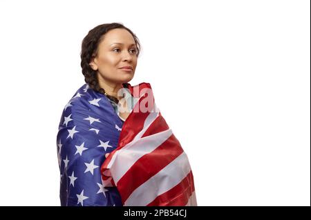 Fière femme multiethnique enveloppée dans le drapeau des États-Unis d'Amérique, regardant loin sur un fond blanc isolé Banque D'Images