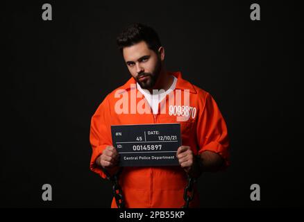 Prisonnier avec des mains chaînées tenant un panneau de lettres de migshot sur fond noir Banque D'Images