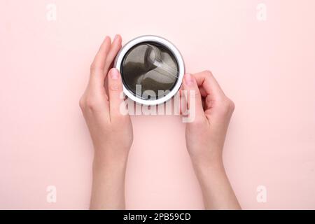 Femme prenant sous le timbre oculaire avec la spatule hors du pot sur fond rose clair, vue de dessus. Produit cosmétique Banque D'Images