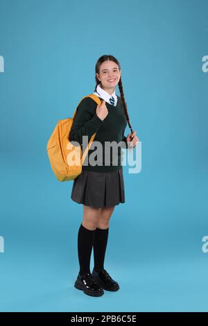 Adolescente en uniforme scolaire avec sac à dos sur fond bleu clair Banque D'Images