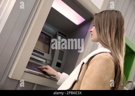 Jeune femme entrant le code PIN de la machine à billets à l'extérieur Banque D'Images