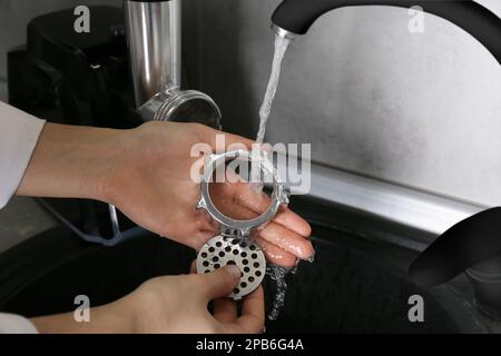 Femme lavant des pièces du moulin à viande électrique sous l'eau du robinet dans l'évier de cuisine à l'intérieur, gros plan Banque D'Images