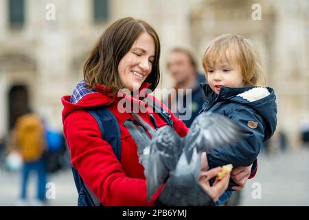 Une jeune mère et son fils qui nourrissent les pigeons sur la place de la cathédrale ou la Piazza del Duomo, dans le centre de Milan, en Lombardie, en Italie. Banque D'Images
