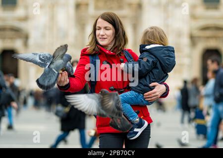 Une jeune mère et son fils qui nourrissent les pigeons sur la place de la cathédrale ou la Piazza del Duomo, dans le centre de Milan, en Lombardie, en Italie. Banque D'Images