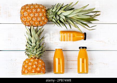 Deux ananas et un smoothie frais et sain dans une bouteille de verre sur fond de bois blanc. Concept de nutrition saine, détox et diététique. Banque D'Images