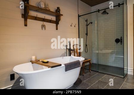 Baignoire sur pied blanche, cabine de douche en verre transparent et céramique dans la salle de bains attenante avec carrelage en ardoise gris nuancé à l'intérieur de la maison hybride en bois. Banque D'Images