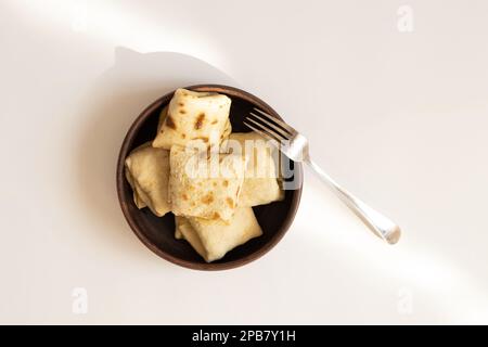 Crêpes farcies dans une assiette en argile avec une fourchette sur un fond blanc au soleil Banque D'Images