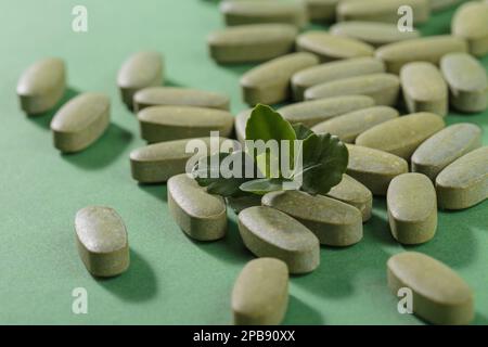 Pilules fines herbes et vitamine Green posées librement sur fond vert Banque D'Images