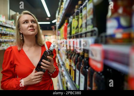 Jeune femme en choisissant l'huile d'olive dans une épicerie. Banque D'Images