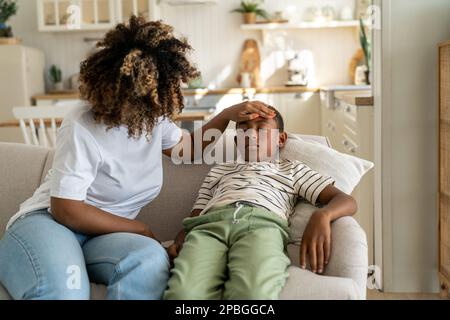 Une mère afro-américaine attentionnée touche le front d'un petit garçon malade Banque D'Images