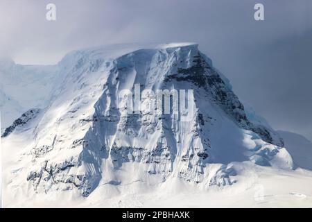 Pic de montagne, péninsule antarctique. Neige, glace bleue, pistes rocheuses. Ciel nuageux en arrière-plan. Banque D'Images