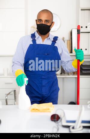 Nettoyant masculin dans un masque de protection et uniforme au bureau Banque D'Images