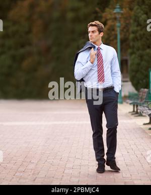 Promenade après le travail dans le parc. Un bel homme d'affaires marchant dehors avec sa veste sur son épaule. Banque D'Images