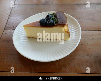 Tranche de tarte au cheesecake recouverte de bleuets sur une assiette, nourriture sucrée avec une table brune en arrière-plan Banque D'Images