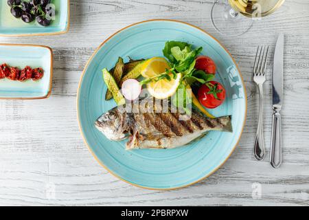 Dorade grillée avec légumes et légumes verts sur une table en bois Banque D'Images