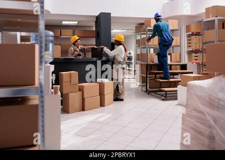 Les employés des entrepôts industriels travaillant dans les entrepôts, gérant l'approvisionnement en stocks. Divers employés de l'entrepôt travaillent en équipe pour balayer les codes à barres des marchandises au comptoir de réception et pour rechercher des colis sur la tablette Banque D'Images