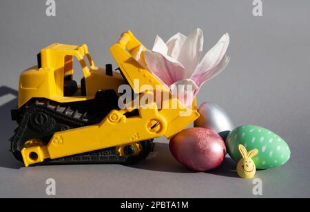 bouteur orange oy, fleur de magnolia, œufs de pâques colorés, lapin de pâques sur fond gris. Happy Easter concept pour les affaires, construction compani Banque D'Images