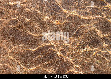 Texture transparente de la surface de la mer d'eau claire avec des ondulations sur une plage de sable avec galets. Arrière-plan abstrait de l'été. Copier l'espace Banque D'Images