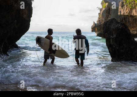 Homme avec une planche de surf va à la tache de surf d'Uluwatu. Banque D'Images