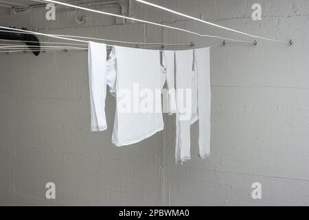 Pyjama blanc ou vêtements suspendus à des lignes de séchage à l'intérieur de la buanderie commune à l'intérieur du bâtiment d'appartement. Personne. Banque D'Images