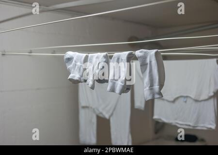 Pyjama blanc ou vêtements et chaussettes courtes accrochées aux lignes de séchage à l'intérieur de la buanderie commune à l'intérieur de l'immeuble d'appartements. Personne. Banque D'Images