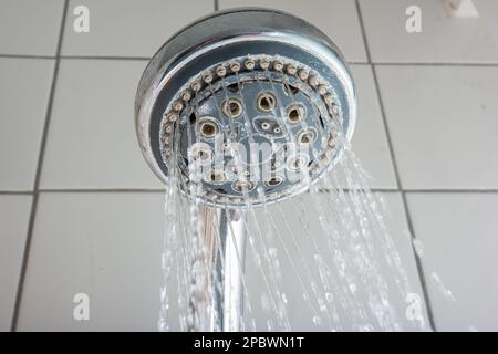 L'eau coule de la pomme de douche ronde argentée dans la salle de bains. Prise de vue en gros plan à faible angle, sans personne. Banque D'Images