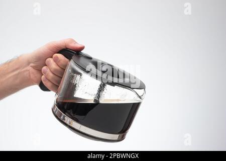 Grande cafetière en verre maison tenue à la main par l'homme faisant un geste versant. Gros plan en studio, isolé sur fond blanc. Banque D'Images