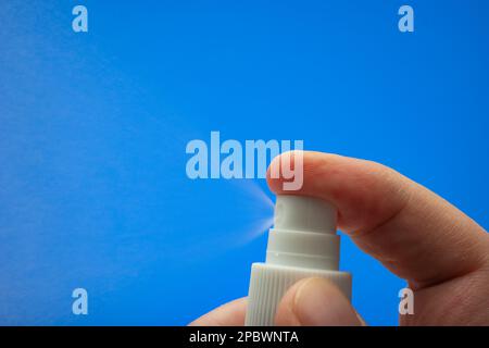 Petite buse de pulvérisateur macro de pulvérisateur tenue par main mâle caucasienne. Gros plan en studio, isolé sur fond bleu. Banque D'Images