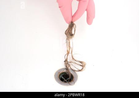 La souche de cheveux mouillés étant enlevée d'une cavité de baignoire par la main mâle dans un gant en latex rose. Gros plan, vue avant. Banque D'Images