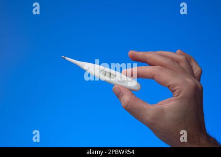 Thermomètre en plastique tenu à la main par un homme caucasien. Gros plan en studio, isolé sur fond bleu. Banque D'Images