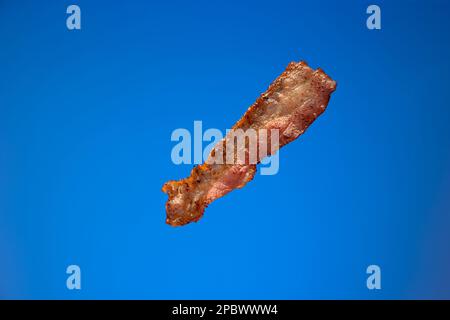 Tranche ou tranche de bacon croustillant. Gros plan en studio, isolé sur fond bleu. Banque D'Images