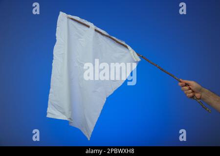 Abandon blanc improvisé ou drapeau de la paix. En bâton de bois et chiffon blanc déchiré. Tenu par une main mâle caucasienne. Gros plan en studio, isolé Banque D'Images