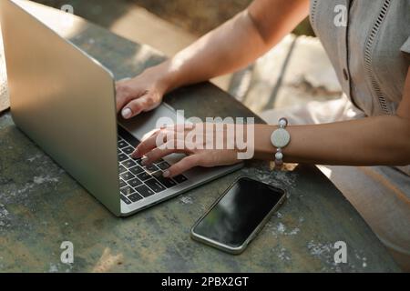 une belle femme mature en chapeau travaille sur un ordinateur à une table blanche dans la nature et passe sa journée productive Banque D'Images