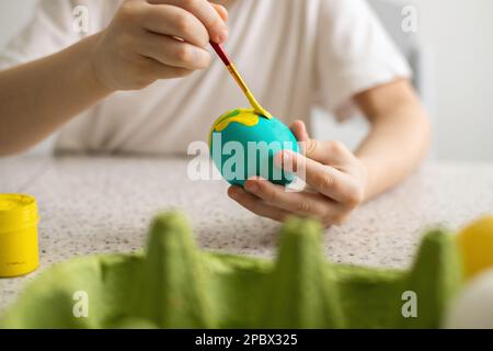 Les mains d'un enfant colorant les œufs avec un pinceau. À proximité se trouvent des peintures et un panier en osier. Gros plan. Pâques Banque D'Images