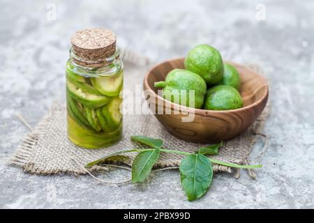 Noix vertes non mûres lisses et teinture de noix dans un pot transparent avec couvercle en liège sur une table ancienne. Feuilles sur la branche de l'écrou. Collecter Banque D'Images