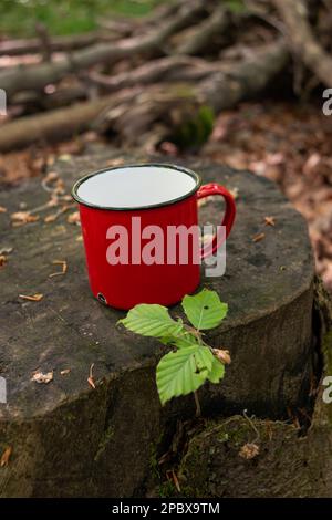 Tasse ou tasse de camping ou de pique-nique en métal rouge. Jour cadre vert forêt, pas de personnes. Banque D'Images