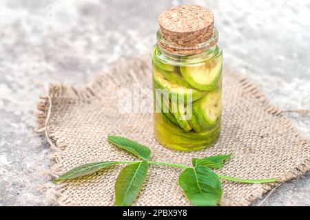 Noix vertes non mûres lisses et teinture de noix dans un pot transparent avec couvercle en liège sur une table ancienne. Feuilles sur la branche de l'écrou. Collecter Banque D'Images