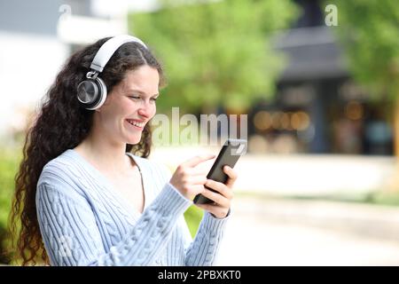 Bonne femme dans la rue à écouter du son sur le téléphone et le casque Banque D'Images