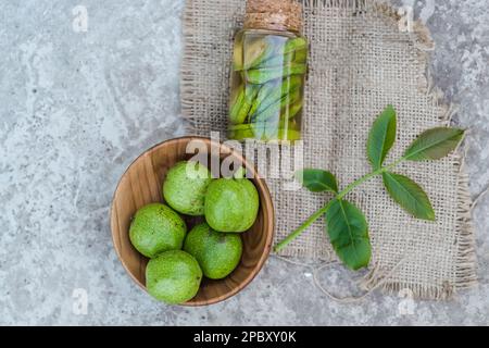 Noix vertes non mûres lisses et teinture de noix dans un pot transparent avec couvercle en liège sur une table ancienne. Feuilles sur la branche de l'écrou. Collecter Banque D'Images