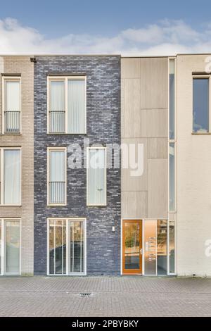 Extérieur d'un bâtiment résidentiel moderne avec fenêtres et portes situé dans la rue de la ville sous un ciel bleu nuageux près d'une passerelle pavée à la lumière du jour Banque D'Images