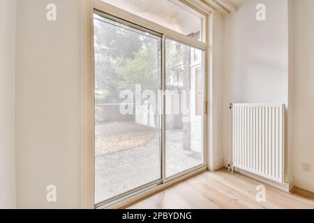 Décoration intérieure de la maison de style contemporain avec portes arrière coulissantes en verre près du radiateur avec cheminée vide et étagère sur le mur avec murs blancs et Banque D'Images