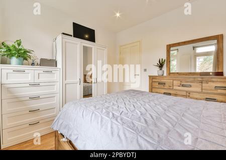 Intérieur d'une chambre moderne avec lit double confortable recouvert d'une housse placée près de commodes en bois avec miroirs dans l'appartement Banque D'Images