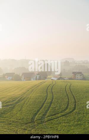 Vue sur le paysage d'un vaste champ avec des sillons situés près du village maisons sous la colline à la lumière du jour dans la campagne avec brouillard loin loin Banque D'Images