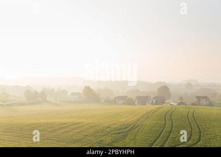 Vue sur le paysage d'un vaste champ avec des sillons situés près du village maisons sous la colline à la lumière du jour dans la campagne avec brouillard loin loin Banque D'Images