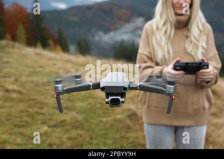 Femme utilisant un drone moderne avec télécommande en montagne Banque D'Images