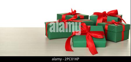 Boîtes-cadeaux vertes avec noeuds rouges sur table en bois sur fond blanc, espace pour le texte Banque D'Images